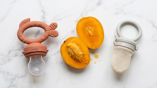 Cubkins BIS Certified silicone fruit feeder teether vs mesh feeder side by side with ripe mango on marble
