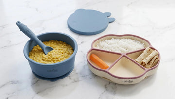 Cubkins blue suction bowl with dal and Raspberry suction plate with Indian finger foods side by side on marble