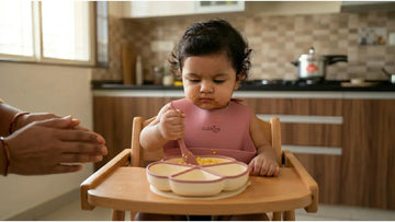 Indian 9-month-old baby self-feeding with silicone bendable spoon from suction plate on highchair tray