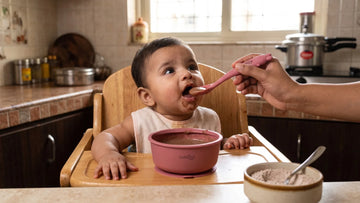 Indian baby eating ragi porridge from a Cubkins raspberry silicone suction bowl