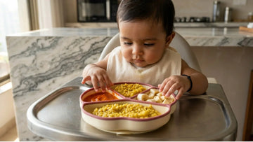 Indian baby pressing hands on raspberry silicone suction plate with khichdi in highchair — Cubkins