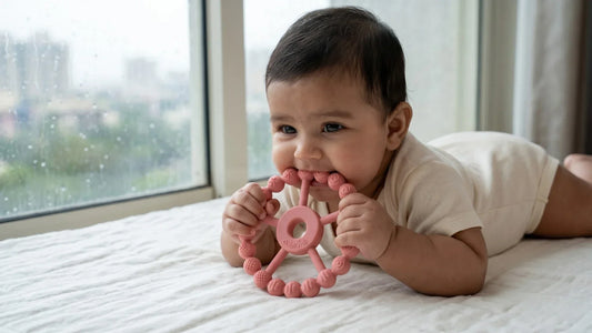 Indian baby holding BIS Certified silicone ring teether in raspberry colour during monsoon — Cubkins