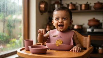 Indian baby wearing raspberry silicone food catcher bib with dal in catch pocket during monsoon weaning — Cubkins
