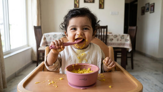 Indian baby learning to hold a Cubkins bendable silicone spoon over a bowl of khichdi