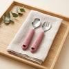 Cubkins raspberry silicone-handle 304 steel toddler spoon and fork on a linen napkin on a wooden tray