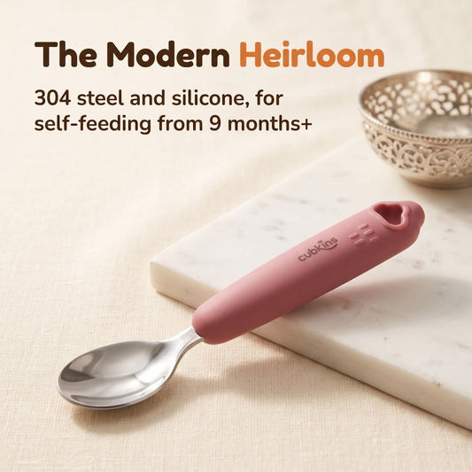Cubkins 304 stainless steel baby spoon with raspberry silicone handle on a marble board beside a silver katori, for self-feeding from 9 months