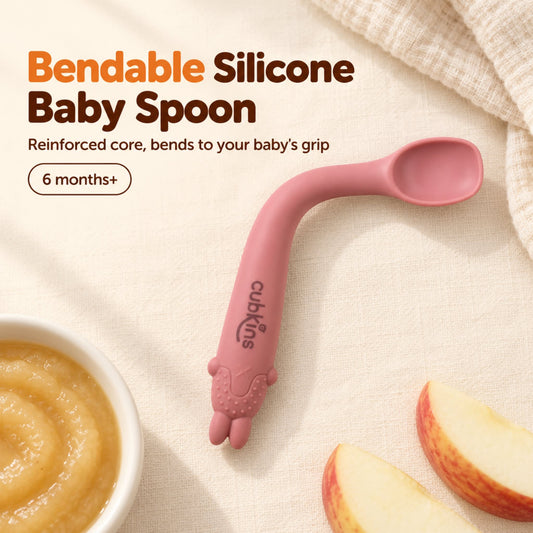 Cubkins raspberry bendable silicone baby spoon with reinforced core, neck bent to a gentle curve, beside apple purée, for 6 months+