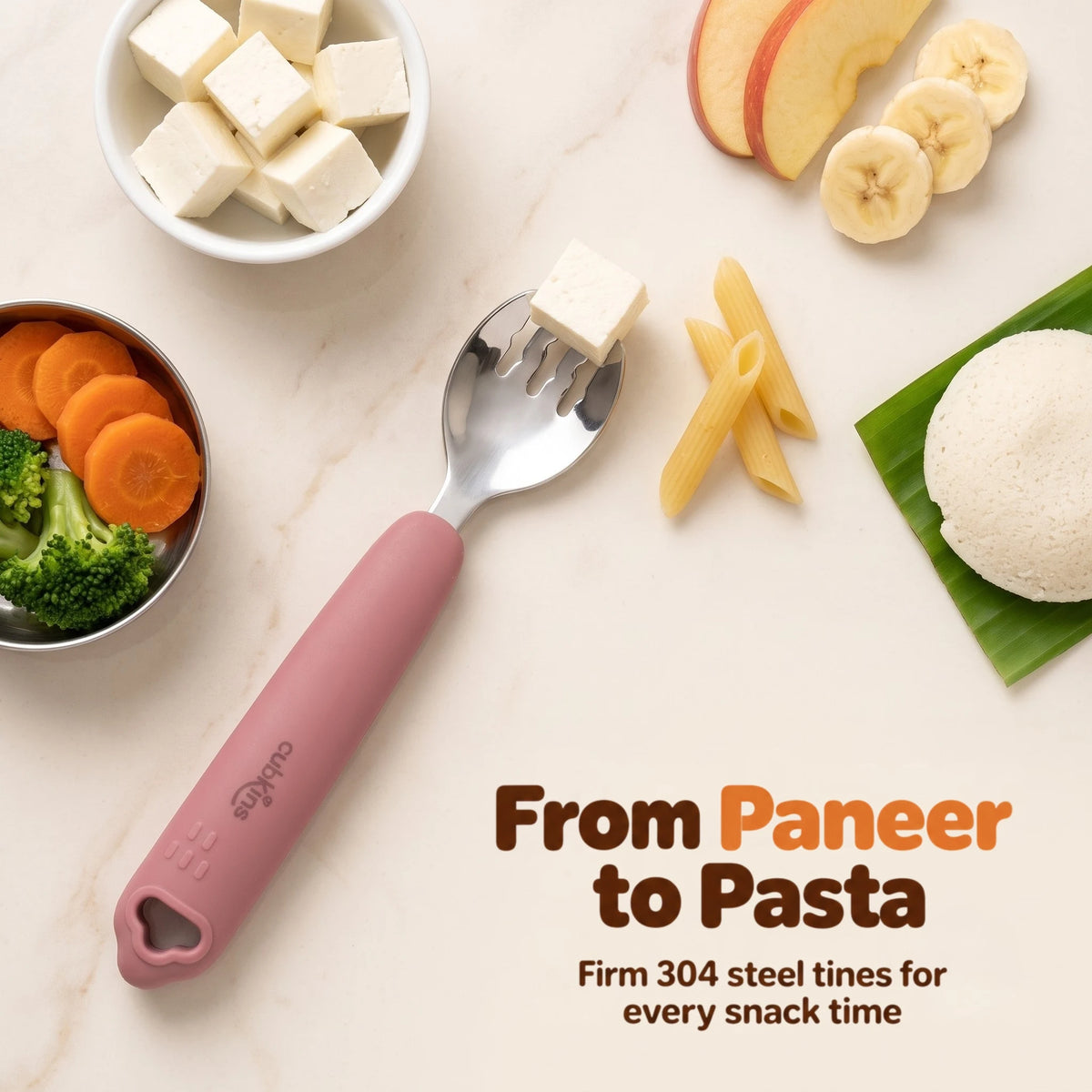 Cubkins raspberry 304 steel toddler fork with a paneer cube on the tines, surrounded by paneer, idli on banana leaf, carrots, broccoli, pasta and fruit