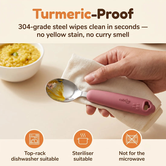 Cubkins 304 steel baby spoon head being wiped clean of turmeric dal, raspberry silicone handle, with care icons for dishwasher, steriliser and no microwave