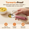 Cubkins 304 steel baby spoon head being wiped clean of turmeric dal, raspberry silicone handle, with care icons for dishwasher, steriliser and no microwave