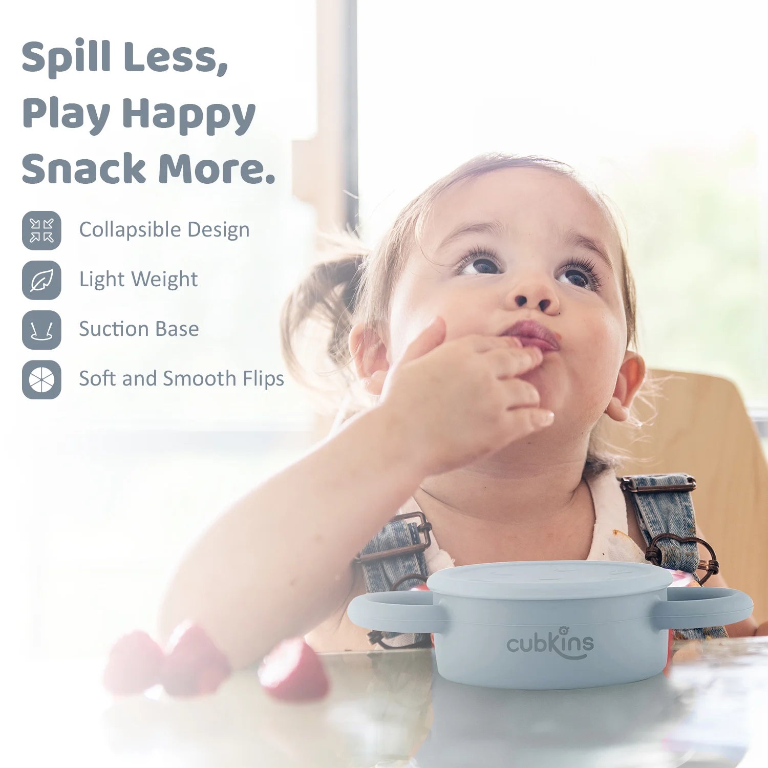 Happy toddler self-feeding from the Cubkins snack cup; features a lightweight design and secure suction base.
