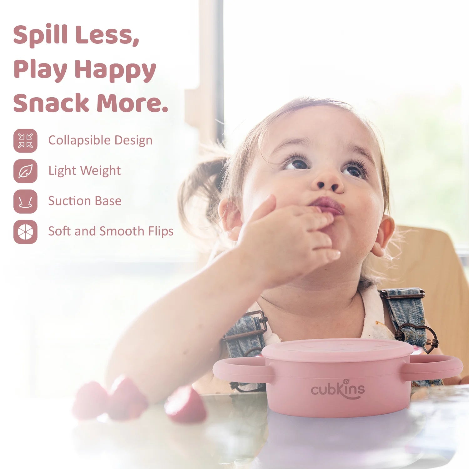 Happy toddler self-feeding from the Cubkins snack cup; features a lightweight design and secure suction base.