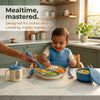 Baby wearing a blue olive Cubkins silicone bib eating from a divided suction plate at mealtime, with suction bowl, sensory straw training cup with transparent window, steel spoon and fork alongside