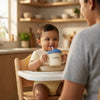 Smiling baby in a high chair drinking from the Cubkins blue olive silicone straw training cup while a parent watches in a warm kitchen setting
