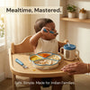 Indian baby self-feeding with Cubkins blue spoon at highchair tray — suction plate loaded with dal, gajar, roti and banana, straw training cup alongside, parent's hand steadying the tray