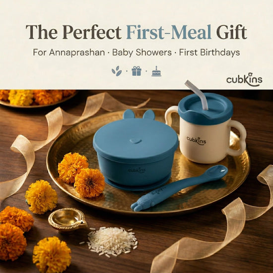 Cubkins blue baby feeding set — suction bowl, training cup, and bendable spoon — arranged on a brass puja thali with marigold flowers and rice, styled as the perfect Annaprashan, baby shower, or first birthday gift.