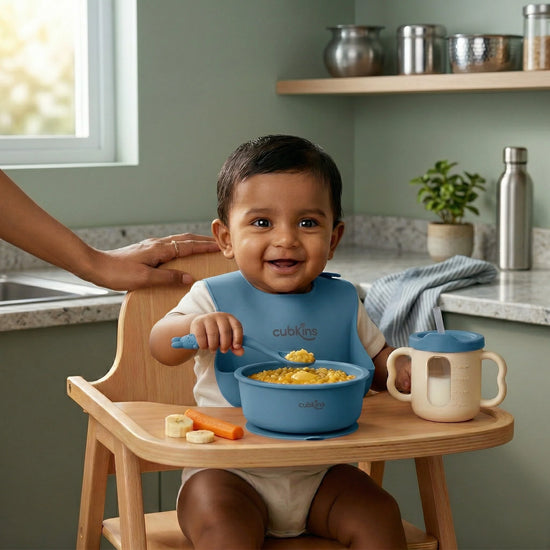 Indian baby in a high chair eating khichdi from a Cubkins blue silicone suction bowl with bendable spoon and training cup on the tray — made for Indian mealtimes.