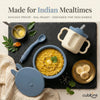 Flatlay of Cubkins blue baby feeding set with khichdi in suction bowl, bendable spoon, and training cup styled on a dark slate board with turmeric, curry leaves, and banana — khichdi-proof, dal-ready.