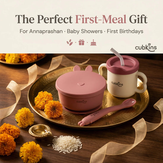 Cubkins raspberry baby feeding set — suction bowl, training cup, and bendable spoon — arranged on a brass puja thali with marigold flowers and rice, styled as the perfect Annaprashan, baby shower, or first birthday gift.