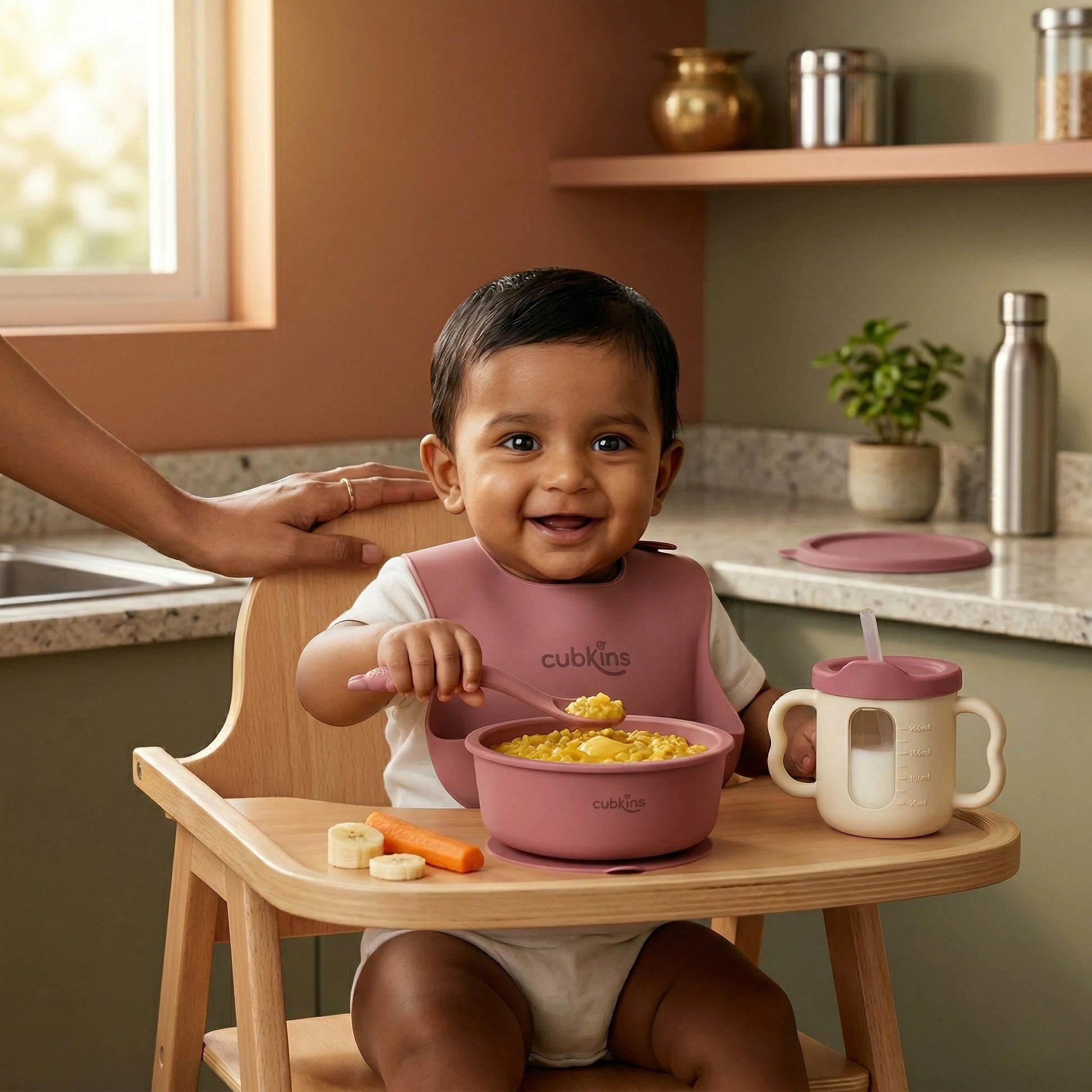 Indian baby in a high chair eating khichdi from a Cubkins raspberry silicone suction bowl with bendable spoon and training cup on the tray — made for Indian mealtimes.