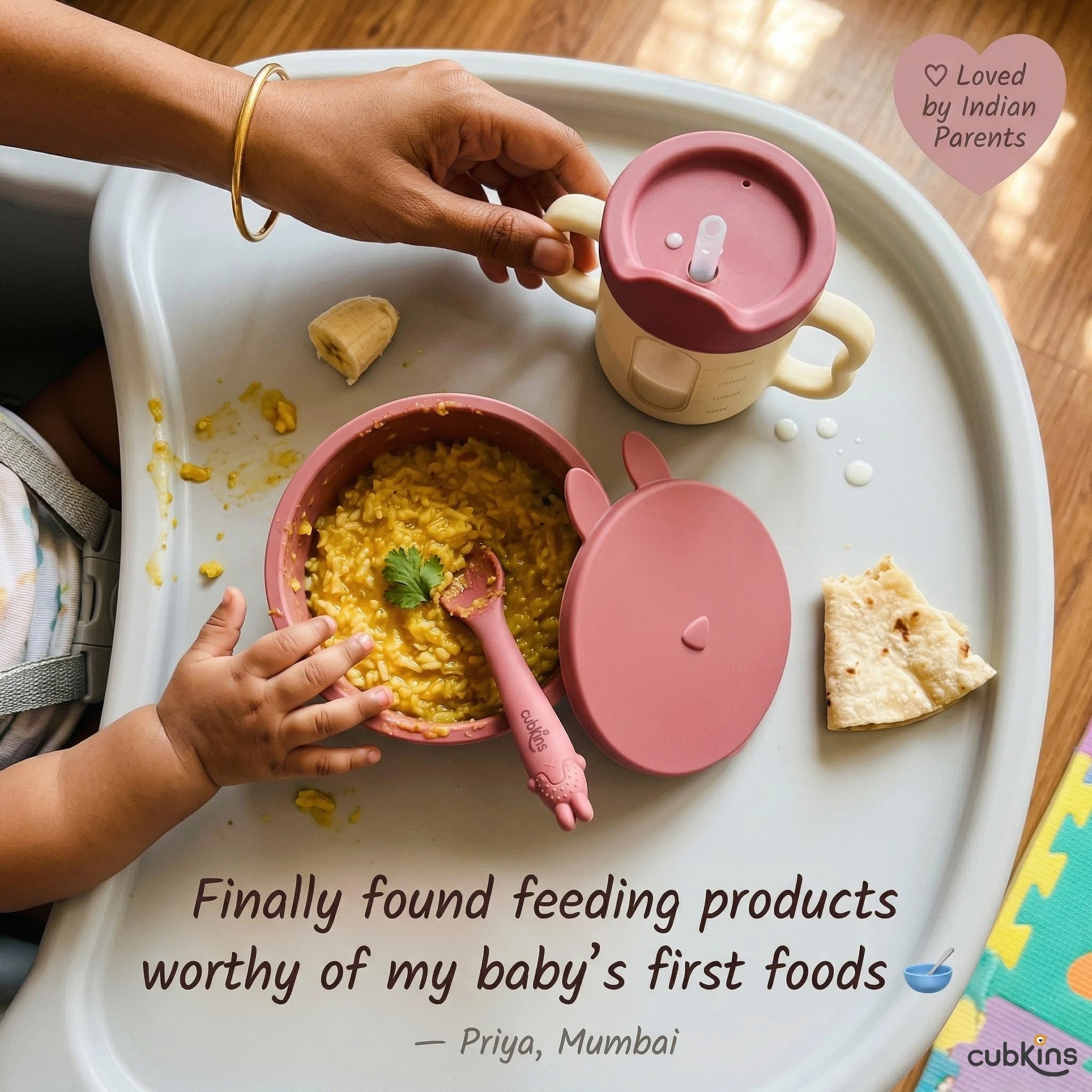 Overhead view of a baby's high chair tray with Cubkins raspberry suction bowl filled with khichdi, roti piece, and training cup — with Indian mom's hand and gold bangle in frame. Quote from Priya, Mumbai.