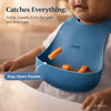 Cubkins blue silicone bib demonstrating stay-open pocket design catching solids and liquids during baby feeding