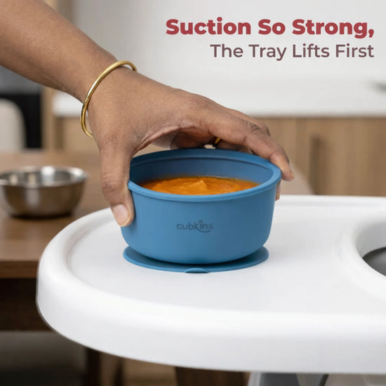 Hand demonstrating strong suction of Cubkins blue baby bowl lifting from white tray with pureed food inside