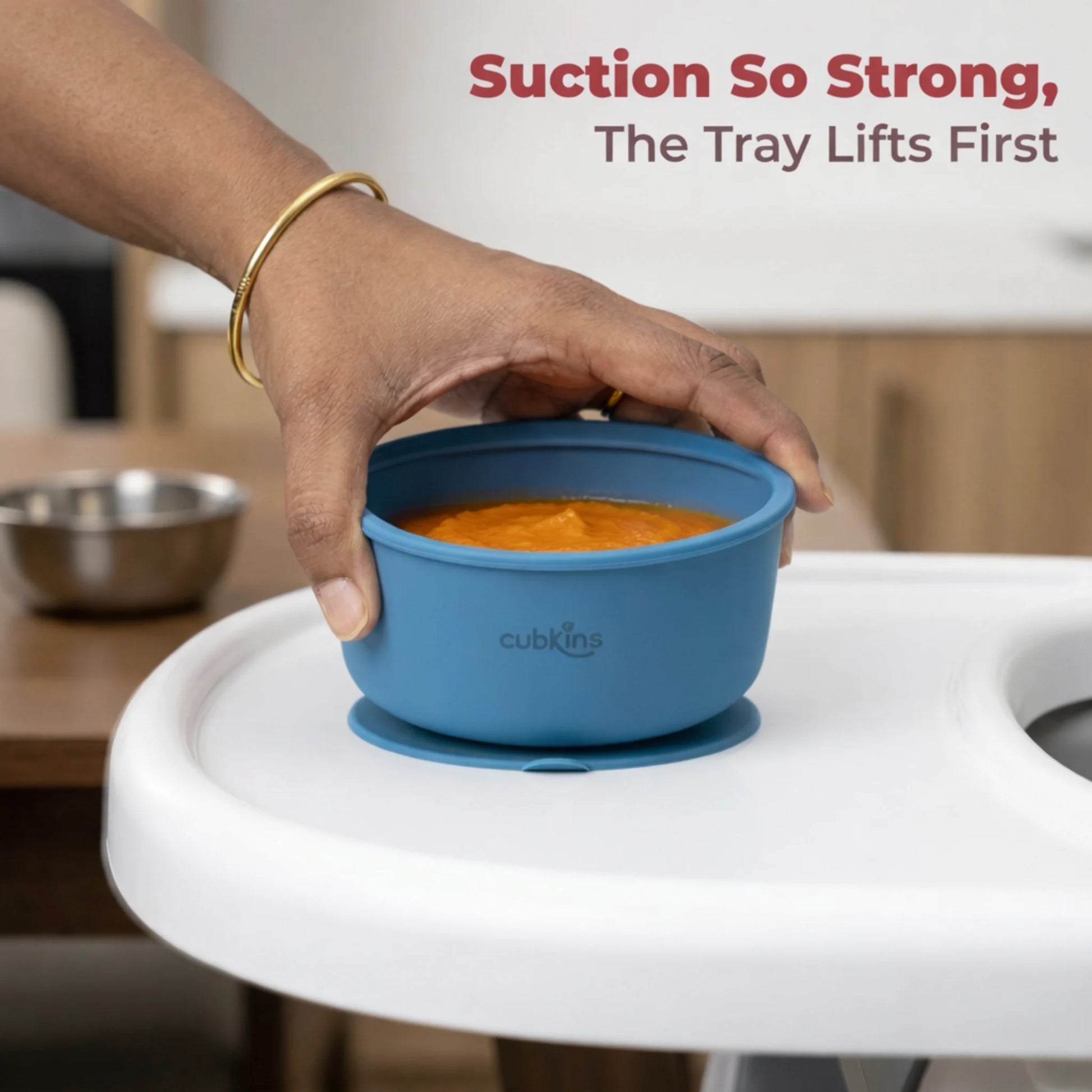 Hand demonstrating strong suction of Cubkins blue baby bowl lifting from white tray with pureed food inside