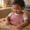 Smiling toddler wearing Cubkins raspberry silicone bib during feeding time, showing comfortable fit and mess-free mealtime