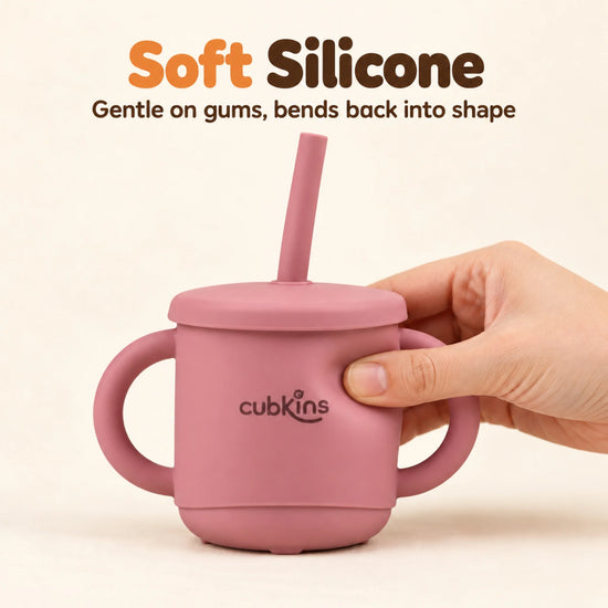 Adult hand gently squeezing the Cubkins raspberry silicone straw cup to show the soft, flexible silicone