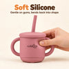 Adult hand gently squeezing the Cubkins raspberry silicone straw cup to show the soft, flexible silicone
