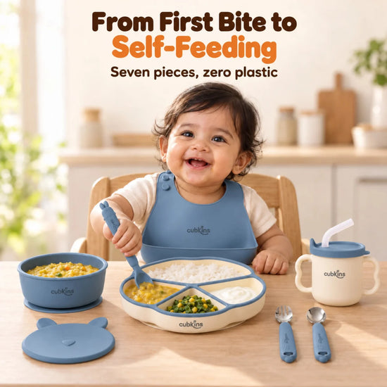 Indian baby at the table with the Cubkins Blue Olive 7-piece feeding set: bib, plate, bowl, bunny lid, sensory straw cup, spoons and fork