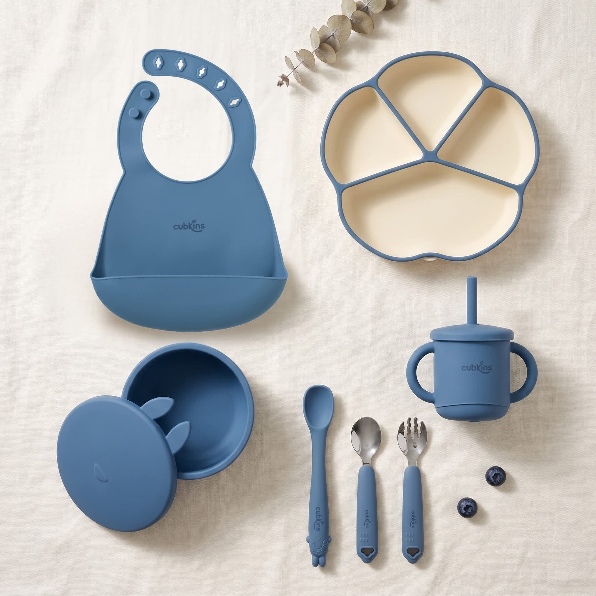 Cubkins 7-piece essential silicone baby feeding set in raspberry pink — bib, 4-compartment suction plate, suction bowl with lid, bendable spoon, steel spoon, steel fork and silicone straw cup laid out flat