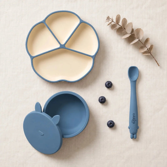 Cubkins plate, bowl and spoon set in Blue Olive: silicone suction plate, suction bowl with bunny storage lid and Smart-Bend bendable spoon, top-down on linen