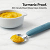 Cubkins steel spoon with blue olive handle being wiped clean of turmeric stain, demonstrating stain resistance
