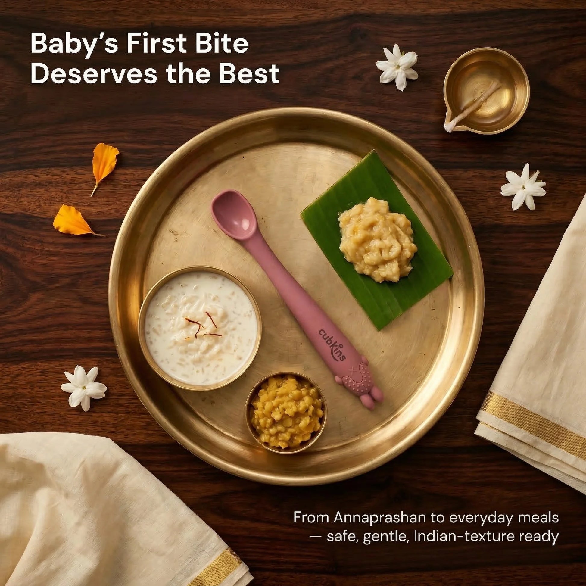Cubkins raspberry silicone baby spoon on a traditional brass Annaprashan thali with payasam, banana mash, and dal, decorated with marigold and jasmine flowers