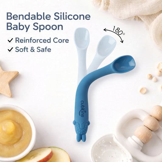 Cubkins bendable silicone baby spoon in blue bending 180 degrees, showing reinforced core and soft safe design, surrounded by baby food and wooden toys