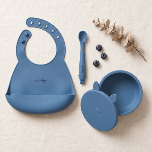 Cubkins feeding set in Blue Olive: silicone suction bowl with its bunny storage lid, silicone bib and Smart-Bend bendable spoon, top-down on linen