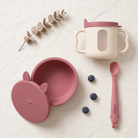 Cubkins feeding set in Raspberry: silicone suction bowl with its bunny storage lid, sensory straw training cup and Smart-Bend bendable spoon, top-down on linen