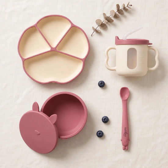 Cubkins complete feeding set of 4 in Raspberry: silicone suction plate, suction bowl with bunny storage lid, sensory straw training cup and Smart-Bend spoon, top-down on linen
