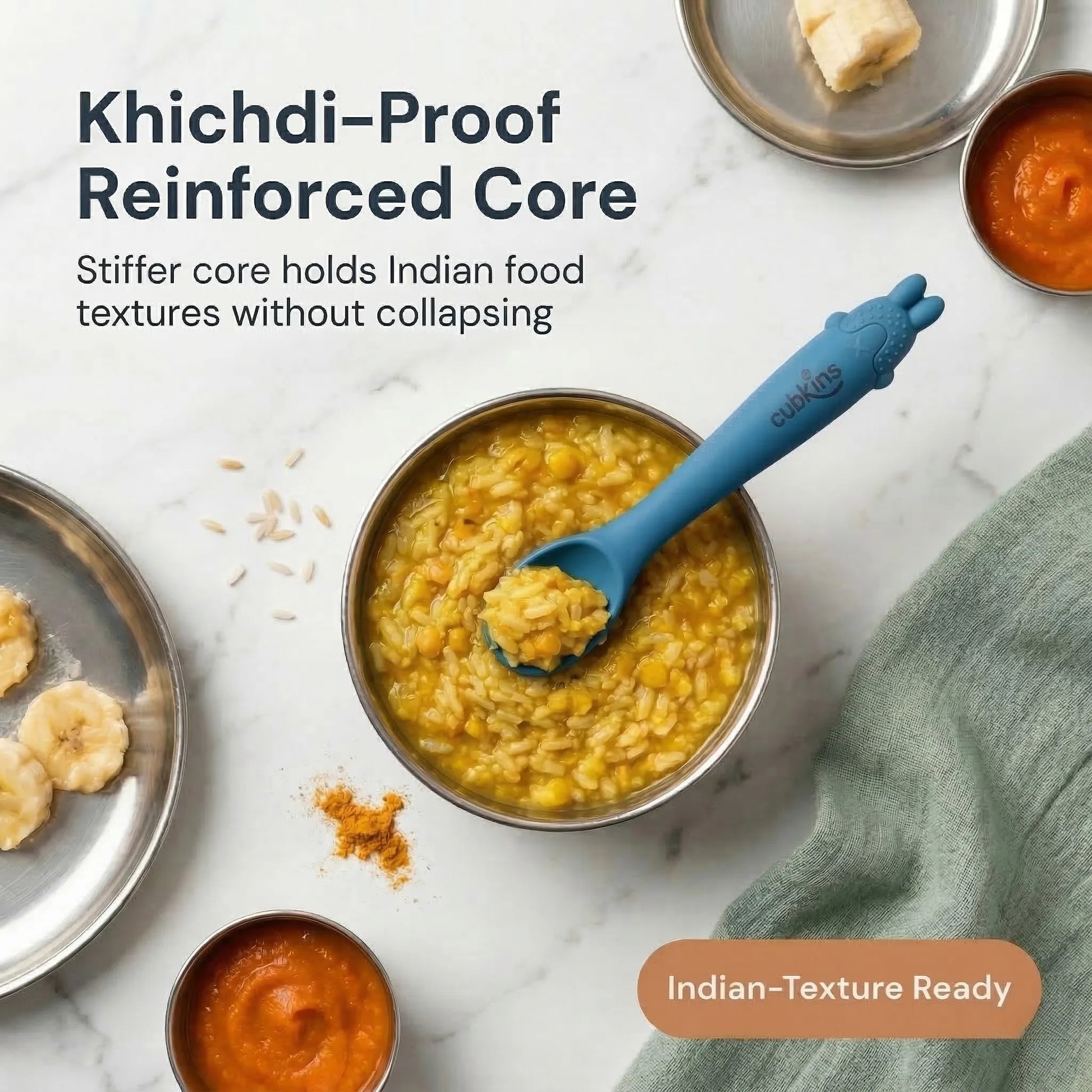 Cubkins blue silicone baby spoon resting in a steel bowl of khichdi, surrounded by Indian baby first foods including banana, dal, and turmeric on a marble surface