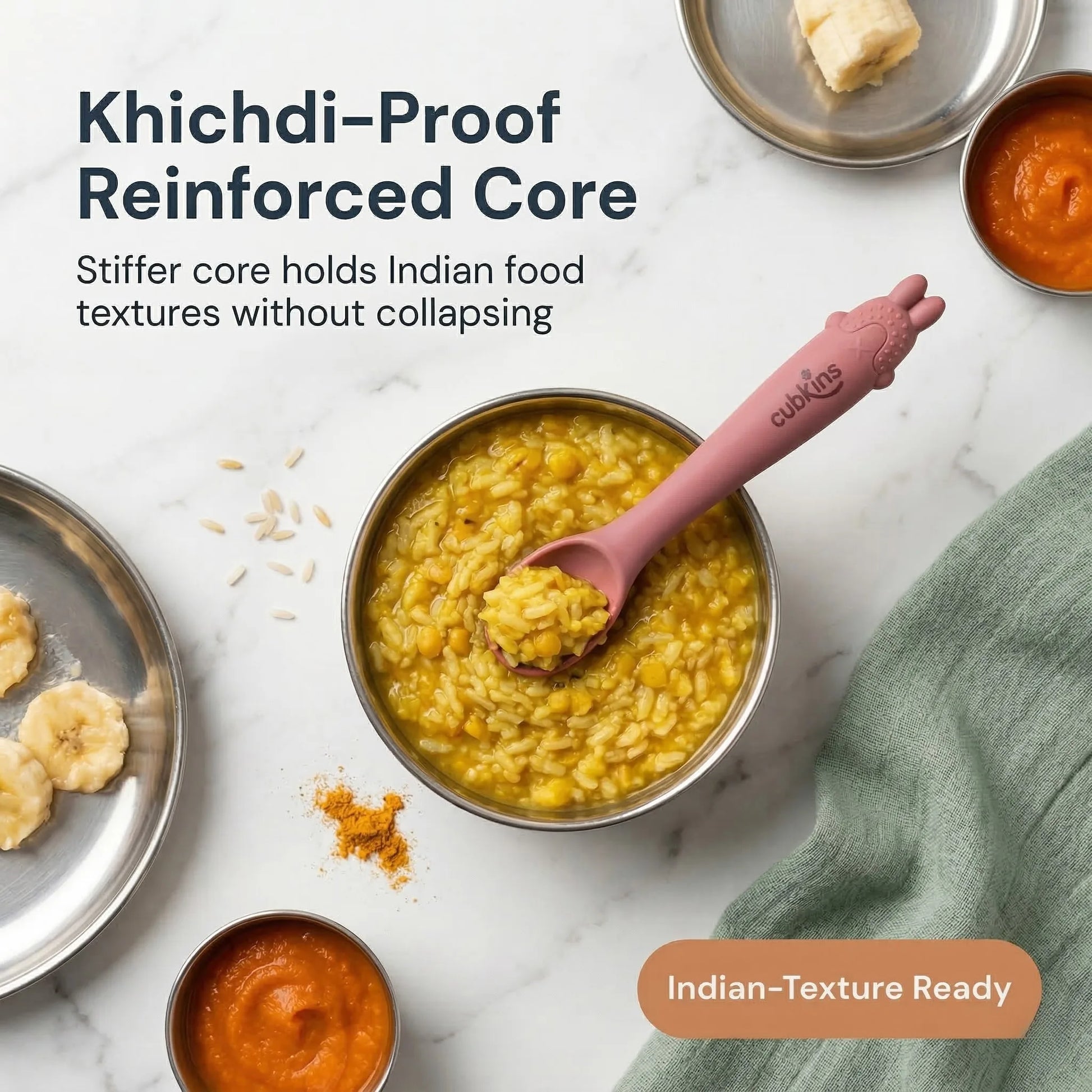 Cubkins raspberry silicone baby spoon resting in a steel bowl of khichdi, surrounded by Indian baby first foods including banana, dal, and turmeric on a marble surface
