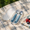 Cubkins blue toddler fork and spoon set displayed inside an open clear travel case on a picnic blanket