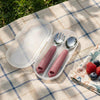 Cubkins raspberry pink toddler fork and spoon set inside an open clear travel case on a picnic blanket
