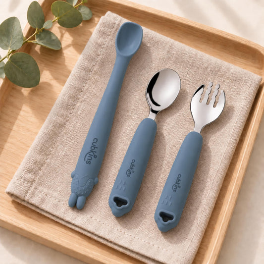Cubkins blue olive self-feeding set of 3: Smart-Bend bendable silicone spoon, 304 steel spoon and steel fork on a linen napkin on a wooden tray