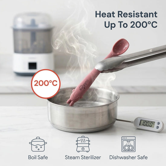 Cubkins raspberry silicone baby spoon being lifted out of boiling water with tongs, showing 200°C heat resistance; icons below confirm boil safe, steam sterilizer, and dishwasher safe.