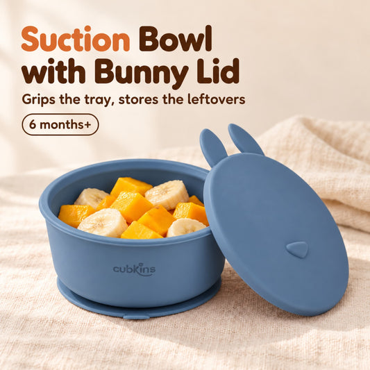 Cubkins blue olive silicone suction bowl with soft mango and banana pieces, its flat bunny-eared storage lid leaning against it, for 6 months+