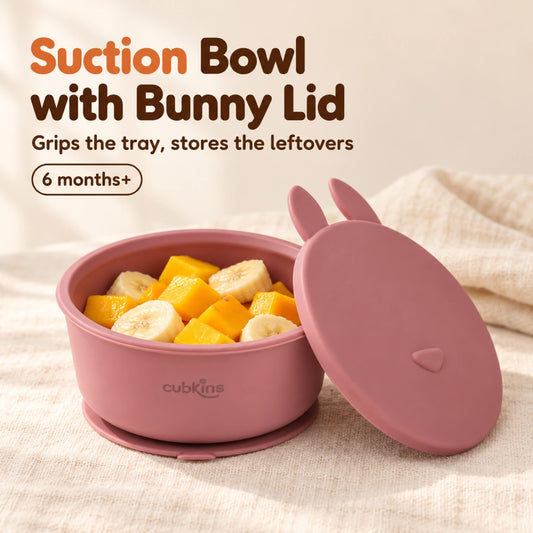 Cubkins raspberry silicone suction bowl with soft mango and banana pieces, its flat bunny-eared storage lid leaning against it, for 6 months+