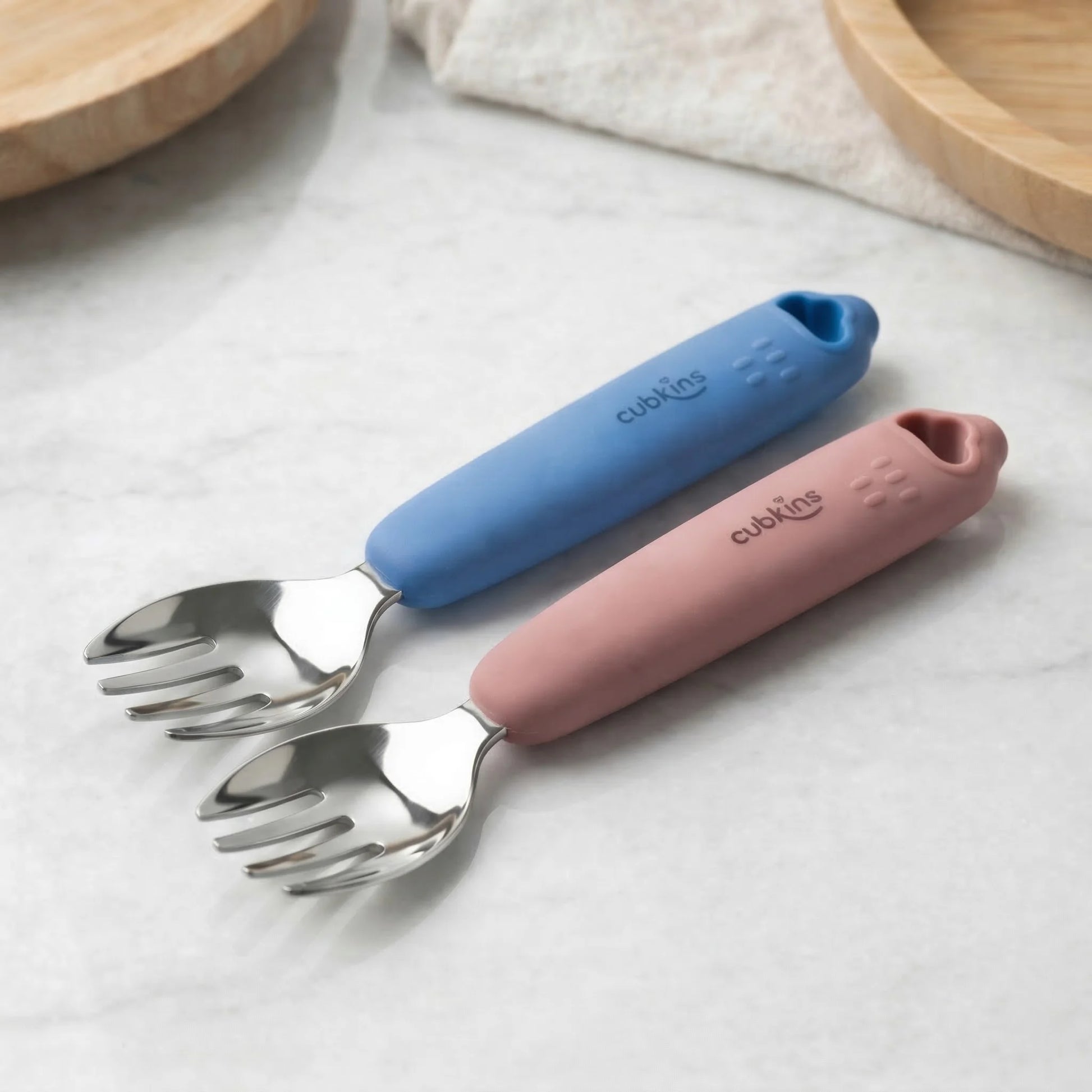Cubkins stainless steel baby fork set of 2 in blue and raspberry silicone handles on marble — both colour variants shown together