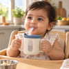 Indian baby in a high chair holding the Cubkins blue olive straw training cup by both handles and drinking water through the straw